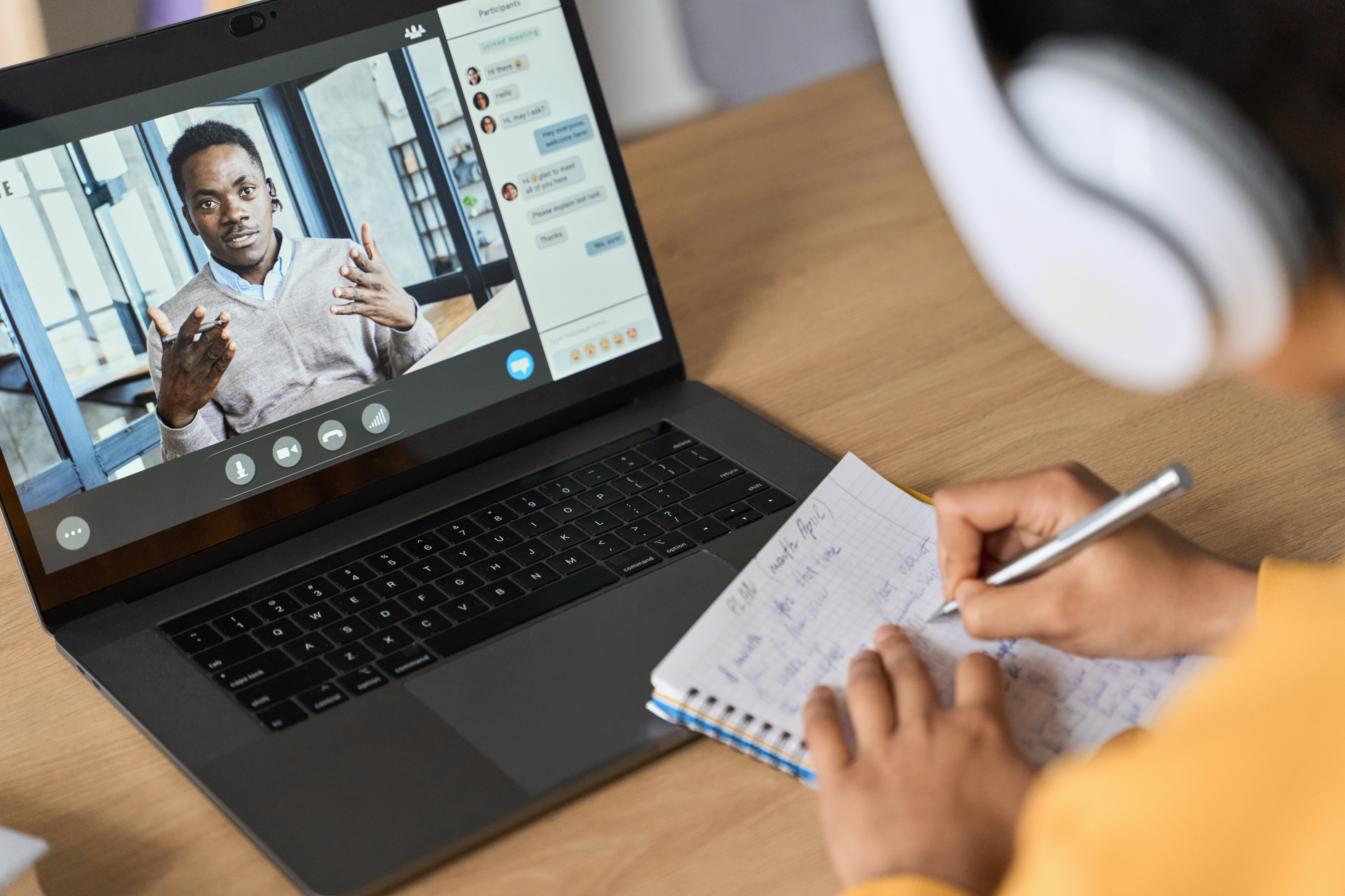 Over shoulder view of female adult student having virtual meeting online call education webinar chatting with black male teacher at home office writing notes. Video elearning conference call on pc.